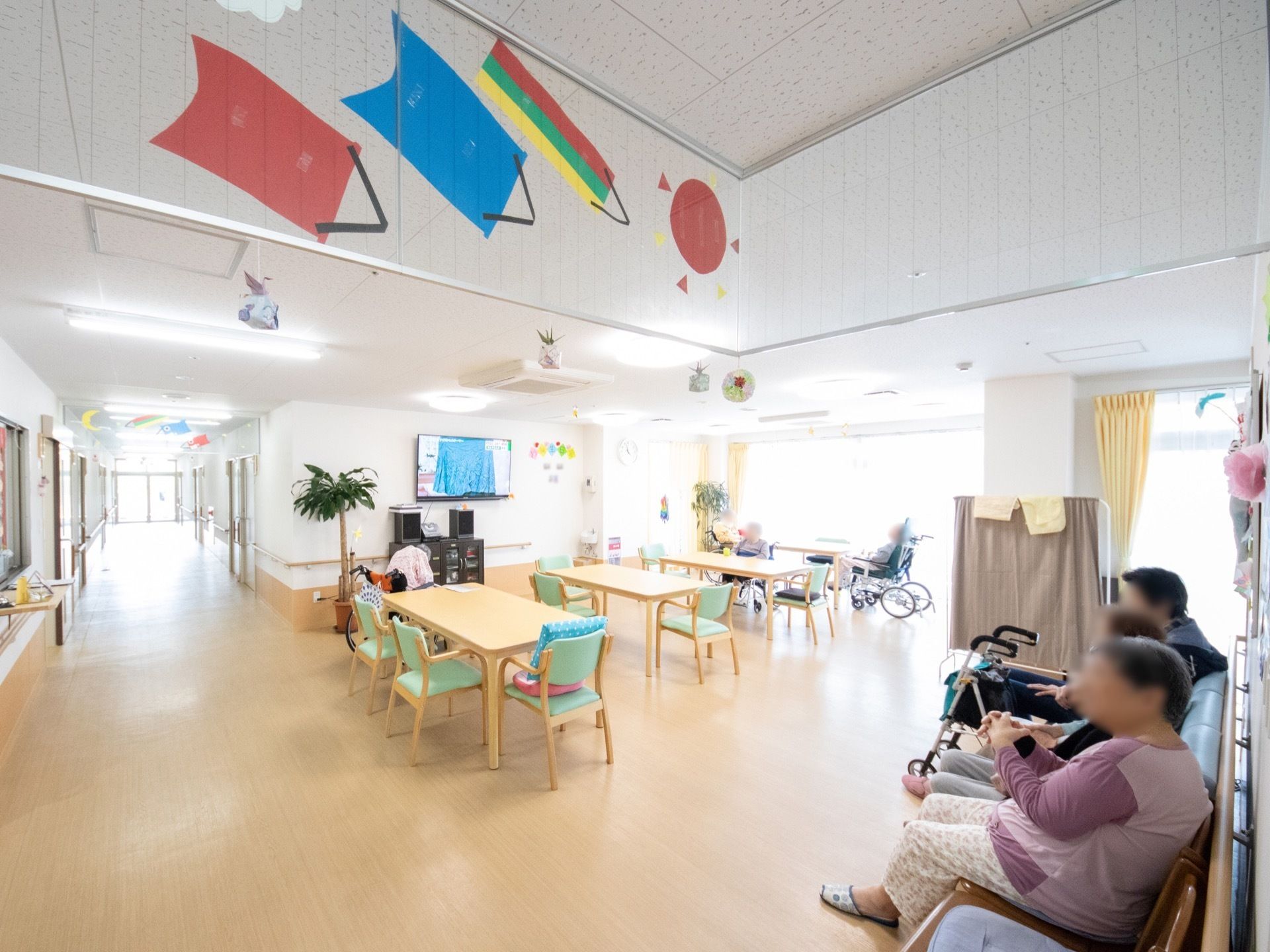 椅子やテーブルだけでなく、テレビも壁に掛けられている。窓からの日差しが明るく、壁に装飾が施されており明るい雰囲気で談笑ができる。