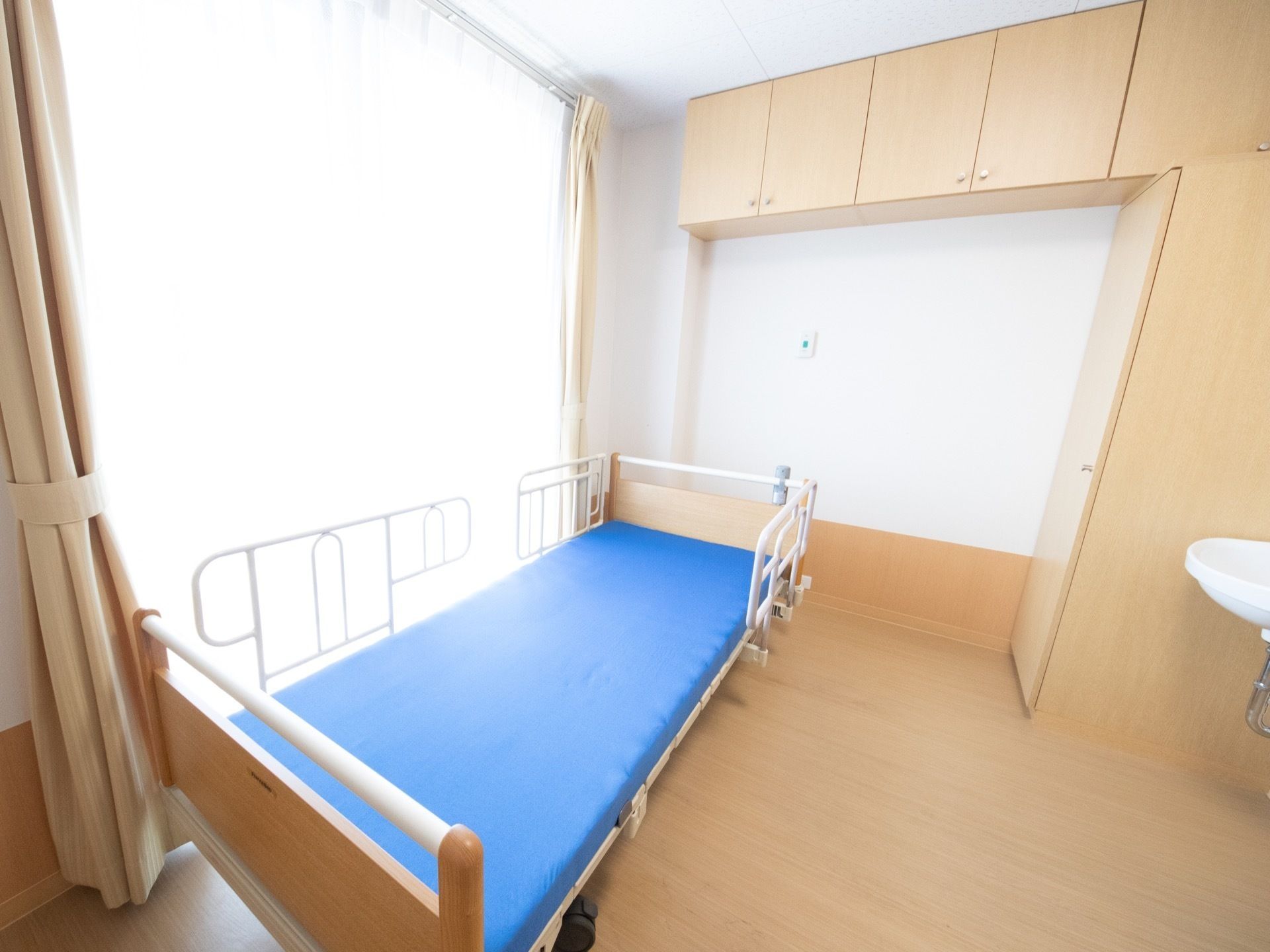 大きな窓から日が差し込む、可動式ベッドと洗面台が設置された居室