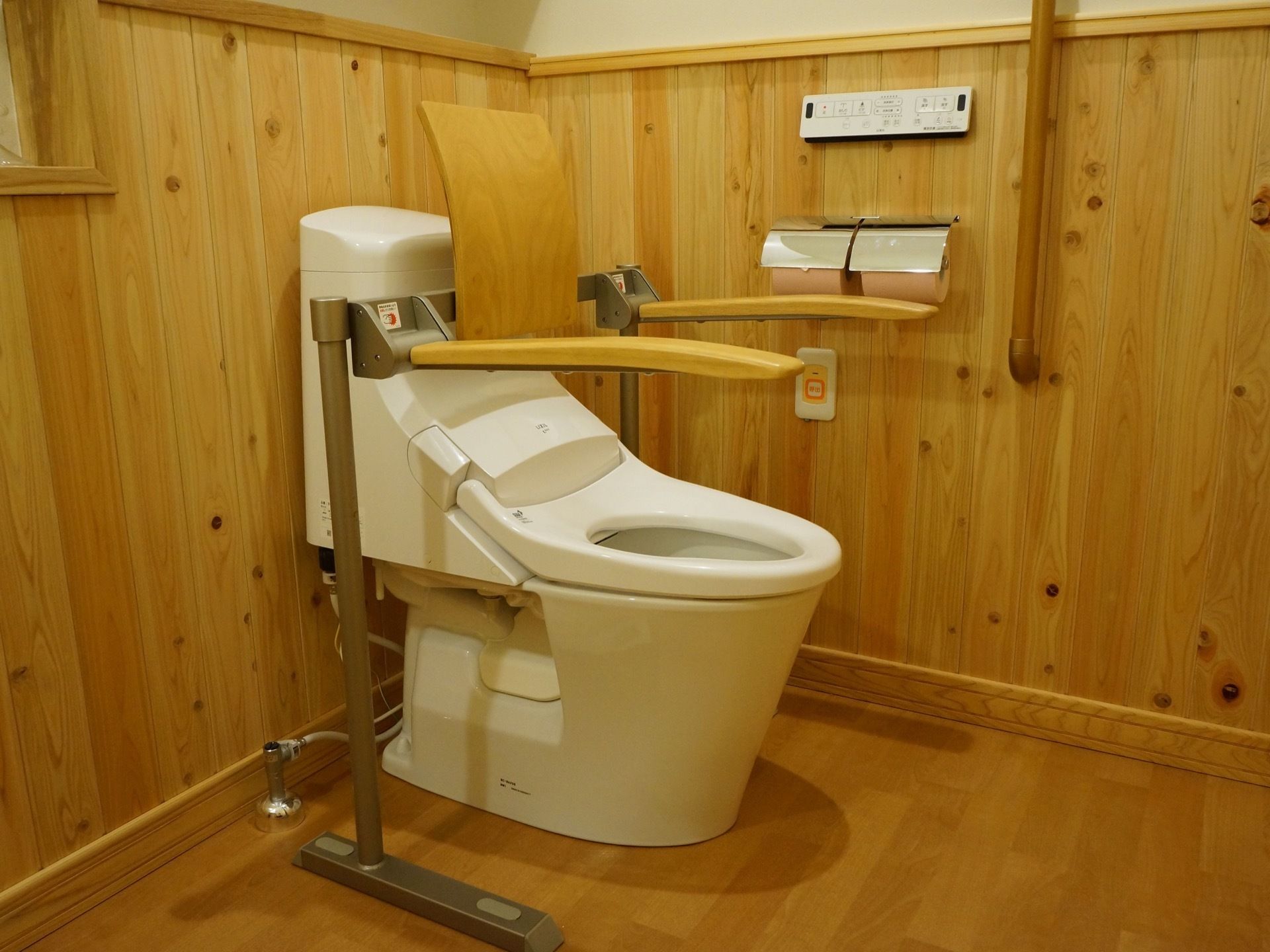 木の温もりを感じるトイレである。背もたれや手すりは木製である。温水洗浄便座器や呼び出しブザーを完備している。