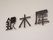 白い壁がある。その壁に、黒い文字で施設名が表示されている。その文字は鉄でできていて、壁から少し浮いている。