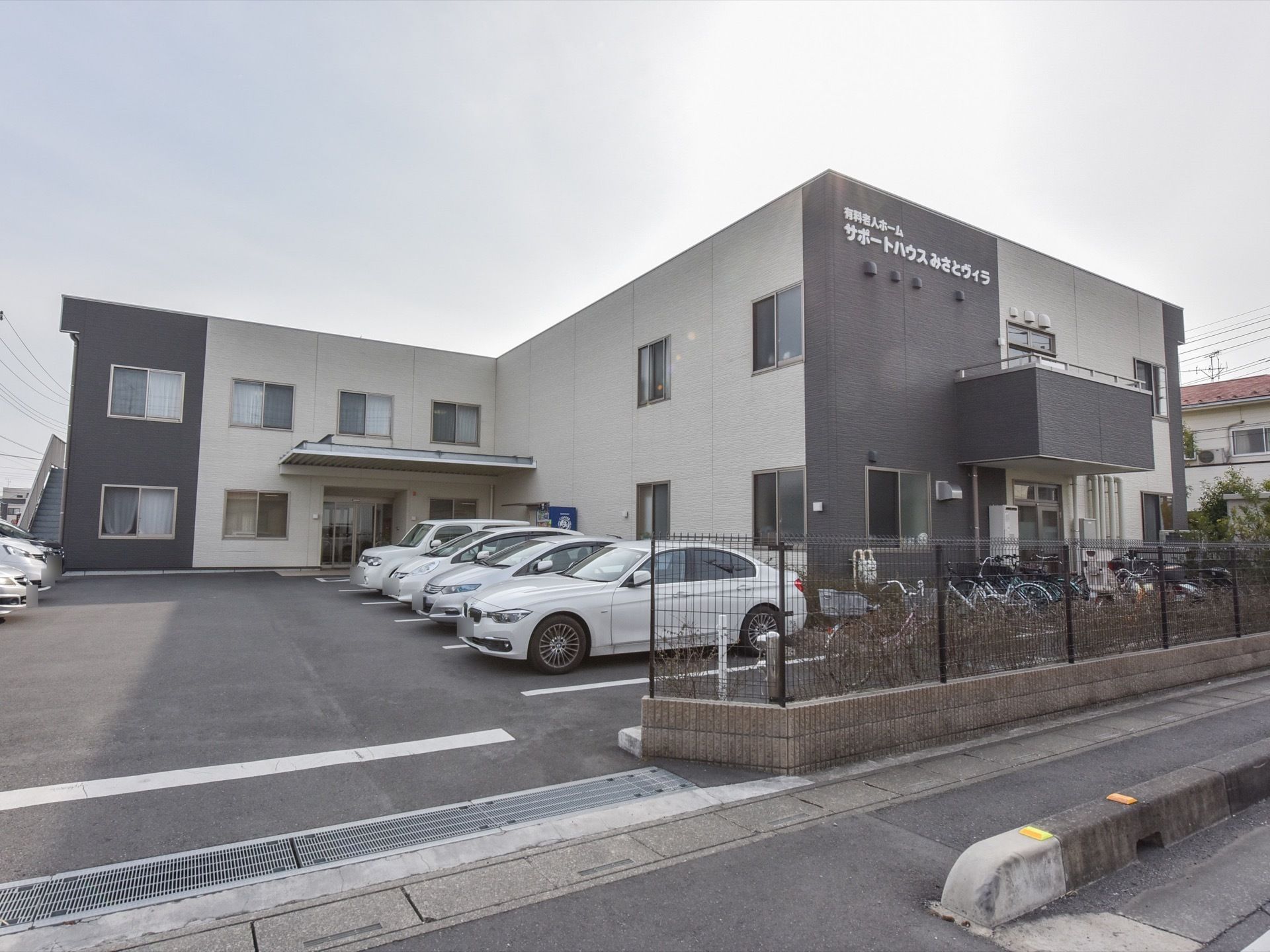 グループホームの建物は２階建てで、ツートンカラーの外壁となっている。また敷地には垣根があり、柵が取り付けられている。