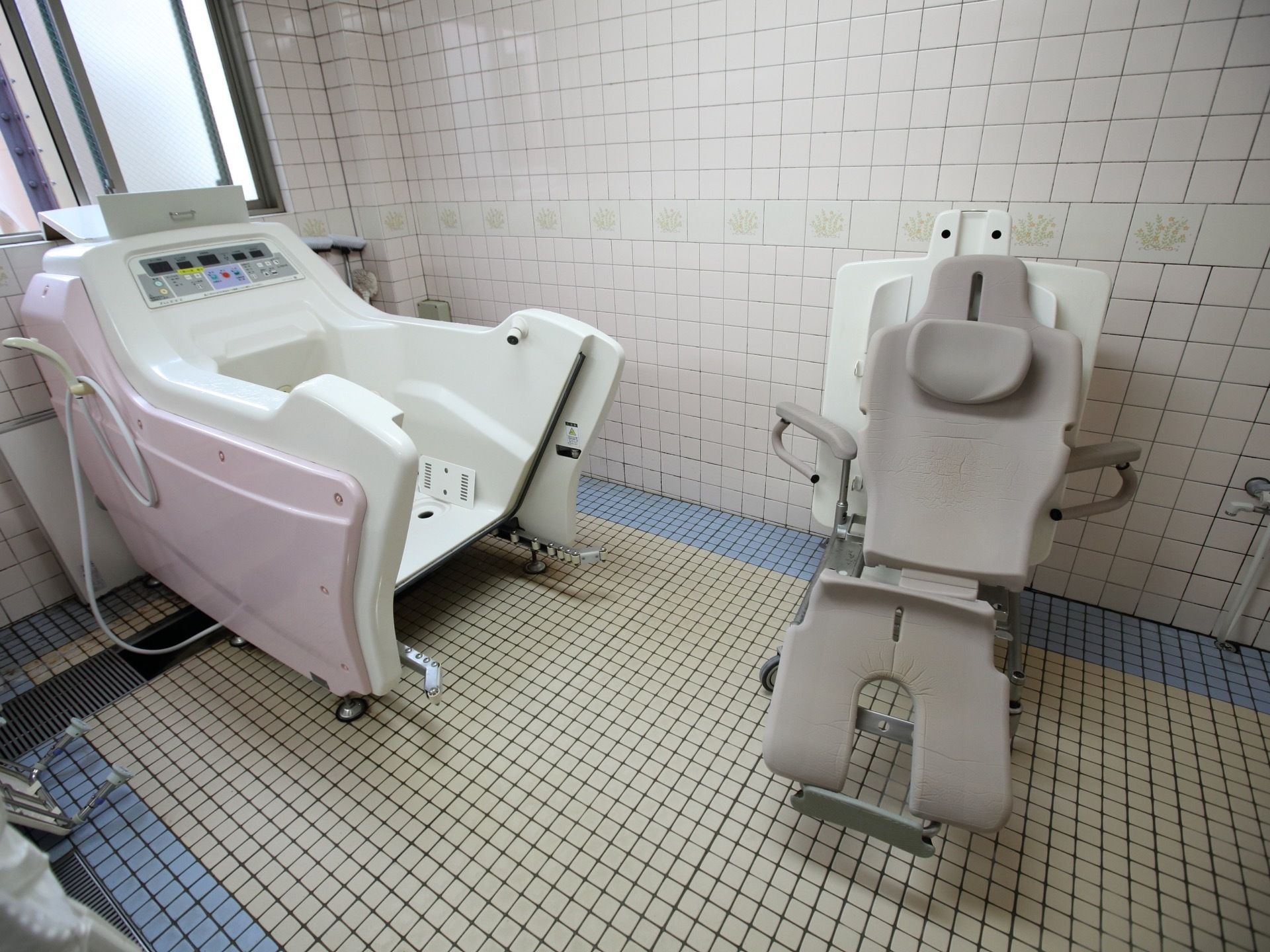 採光窓が付いたタイル張りの浴室がある。広々としていて、グレーのストレッチャーと機械浴槽が置かれている。