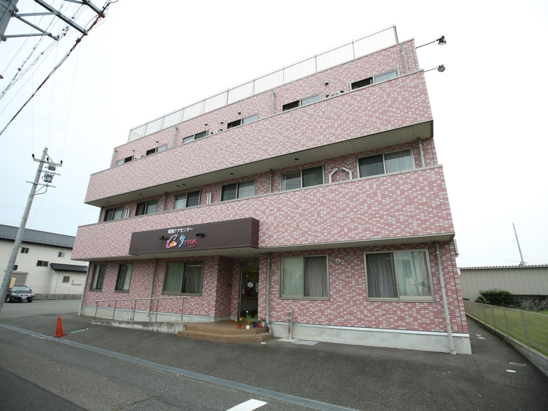 道路に面した場所に３階建ての集合住宅が建っている。敷地は舗装されていて、建物の横は駐車スペースになっている。