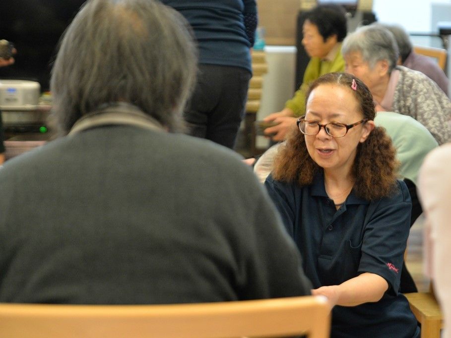 椅子に座っている入居者様にスタッフがしゃがんで話しかけている。入居者様が快適に過ごせるよう心を込めてサポートしている。