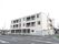 広い道路のある通りに立つ、3階建ての白い建物である。２階と３階には、居室の窓とベランダが並んでいる。