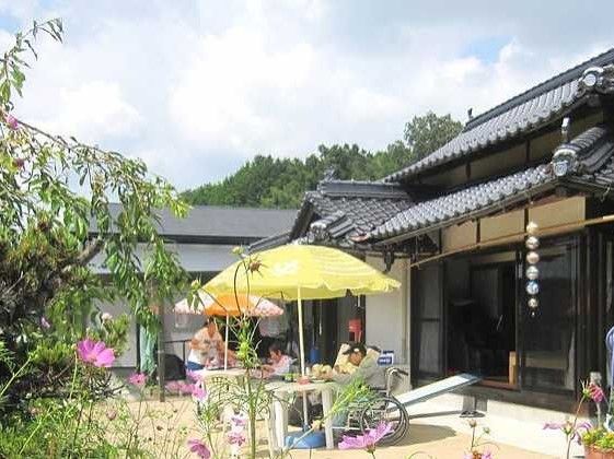 パラソル付きのテーブルが設置された庭で入居者とスタッフがティータイムを楽しんでいる。