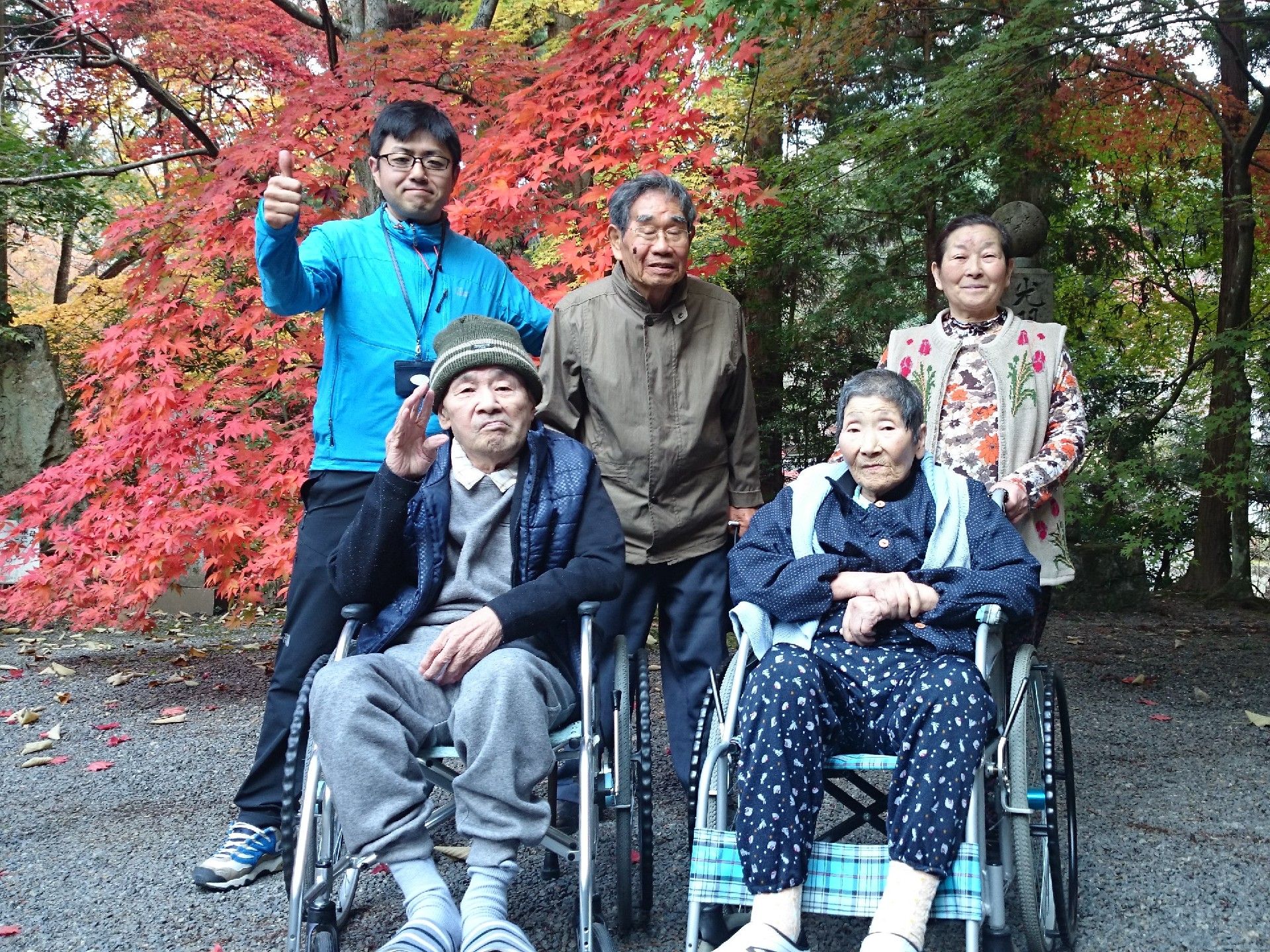 紅葉をバックにポーズをとるスタッフと入居者。車いすを利用している入居者も一緒に。