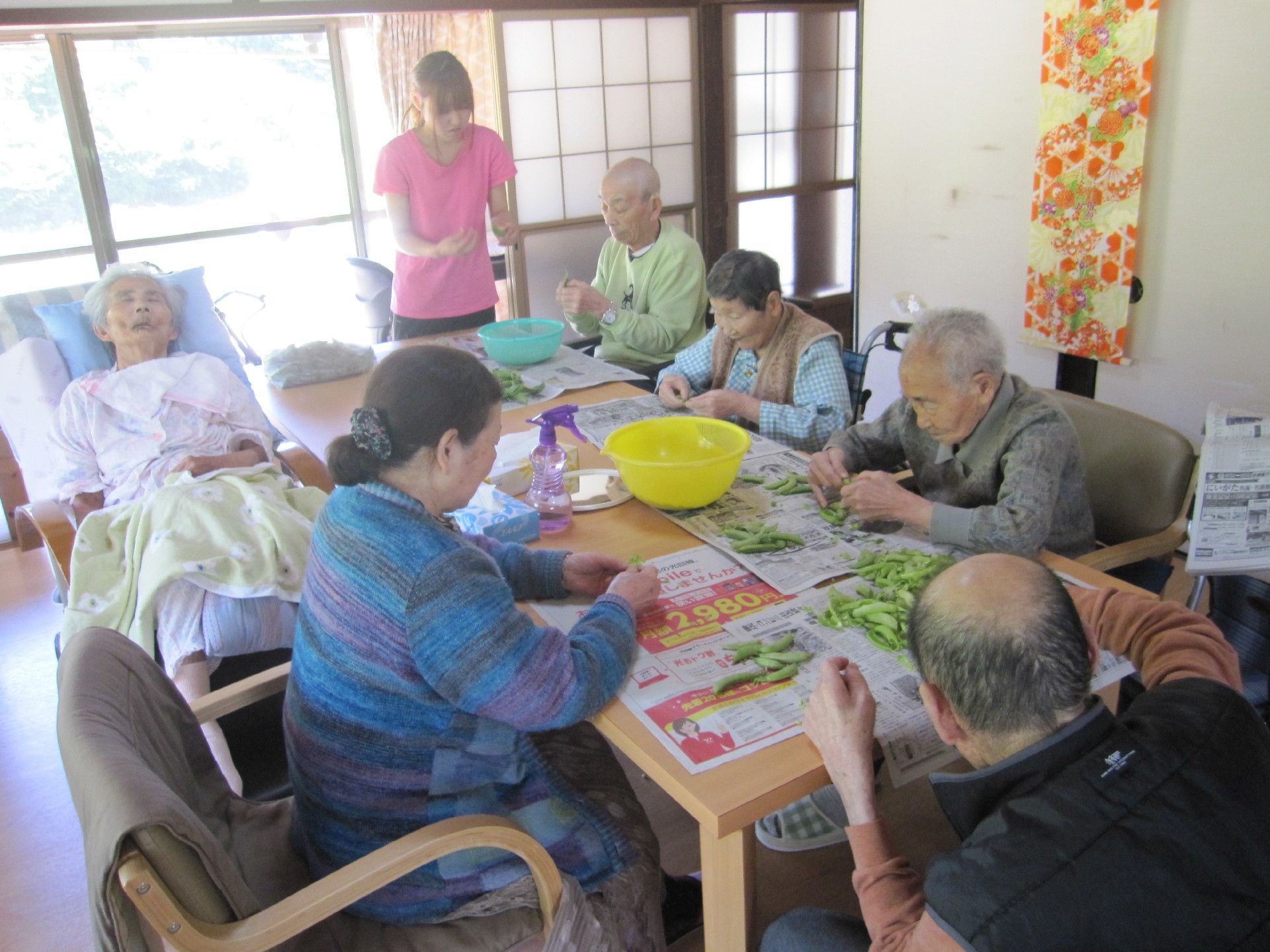 ダイニングテーブルを囲んで野菜の下ごしらえをするスタッフと入居者。