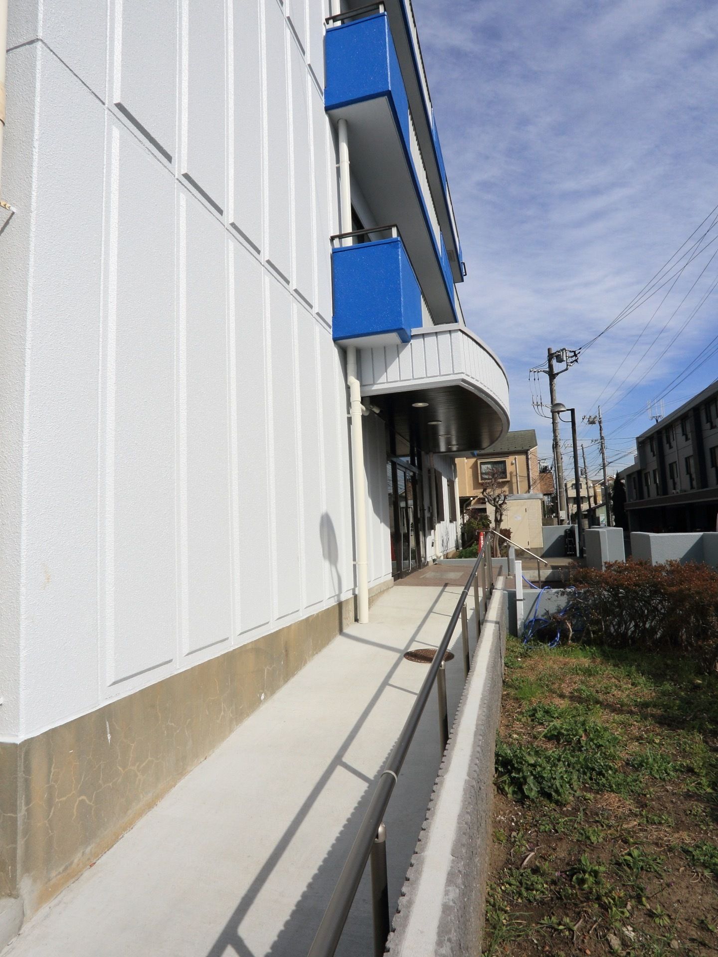 玄関の前から外周に続く通路は平らで手すりがついている。２階と３階のブルーのベランダが鮮やかで目を惹く。