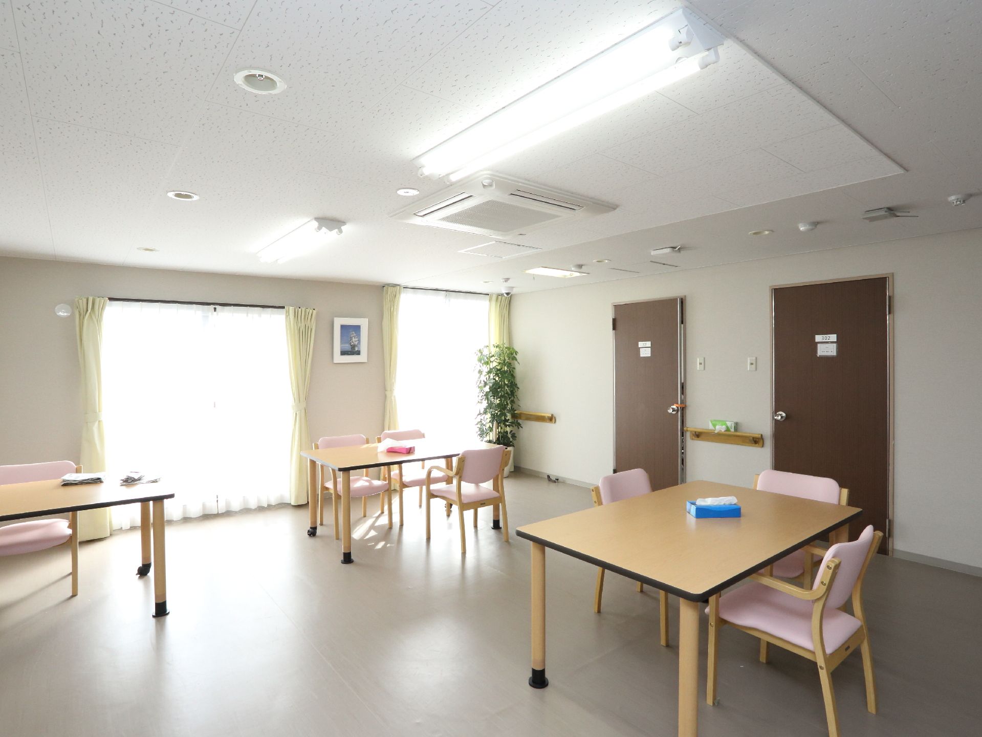 木製のテーブルに薄ピンク色の椅子がセッティングされ、扉が2つある待合スペース