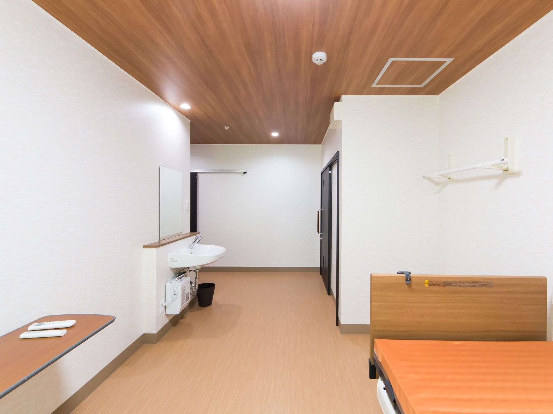居室の天井は木目調で、床面はビニール素材になっている。壁に鏡が取り付けられた洗面台がある。