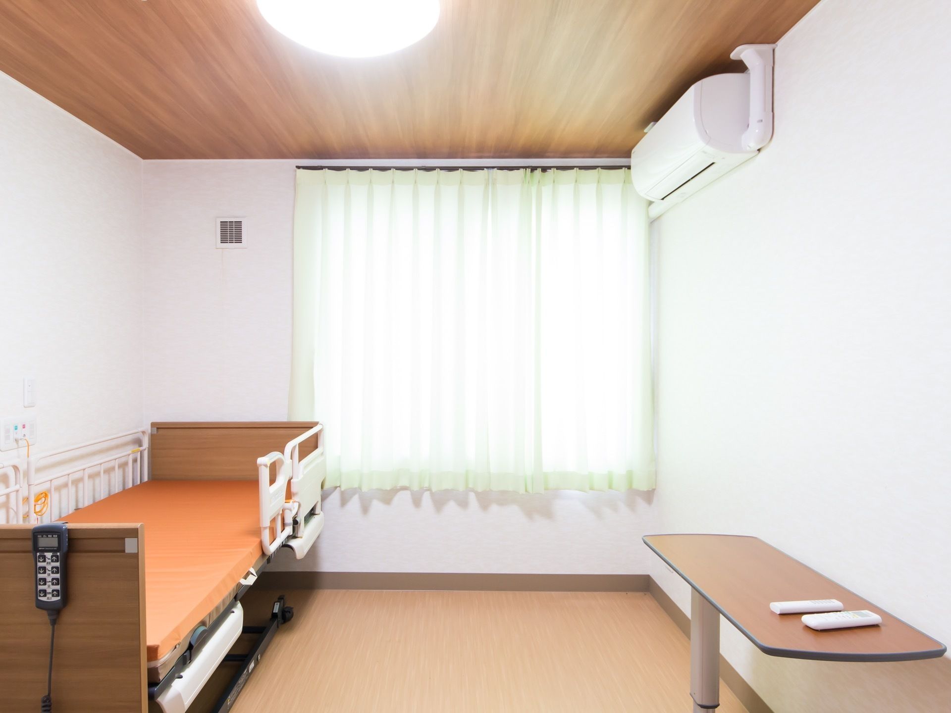 居室に、転落防止柵がついた介護ベッドがある。ベッドの操作のためのリモコンが木の板にかけられている。