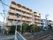 施設の周辺には住宅が立ち並んでおり、建物の前方に歩行者用信号と横断歩道が設置されている。横断歩道の先には橋がある。