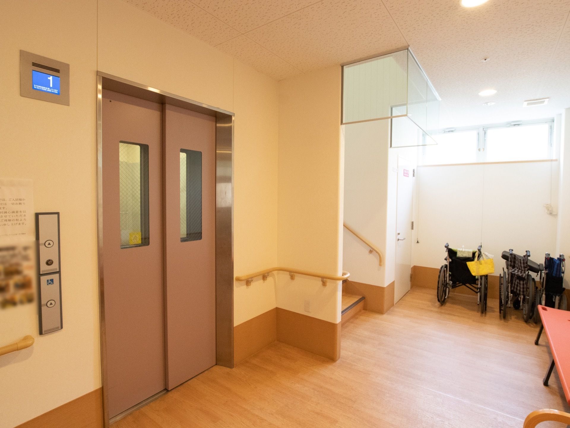エレベーターと階段が並んでおり、壁には手すりが備わっている。エレベーターの扉には縦長の窓がついている。