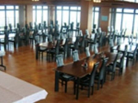 仕切りのない広い部屋で、柱が数本見える。こげ茶色のテーブルが20以上設置され、それぞれ椅子が置かれている。