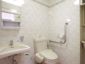 個室内に、手洗い場が一緒になっているタイプのトイレ。奥に洋式便器があり、壁にL字型の手すりが設置されている。