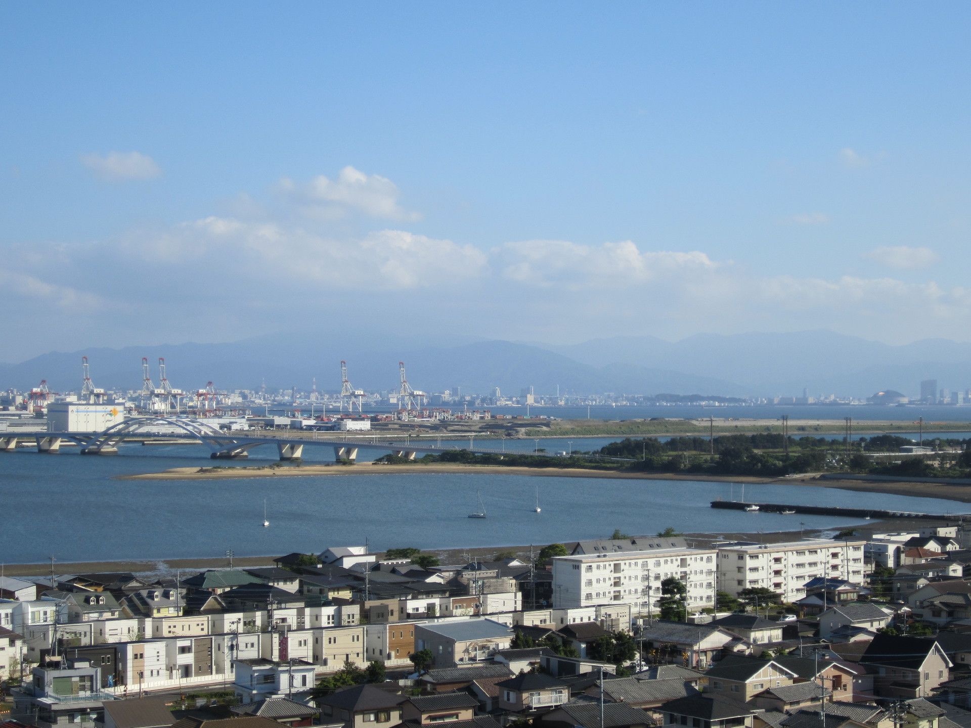 施設から見た外の様子。向こう側に海が広がっていて、橋が架かっている。手前には人家などが立ち並んでいる。