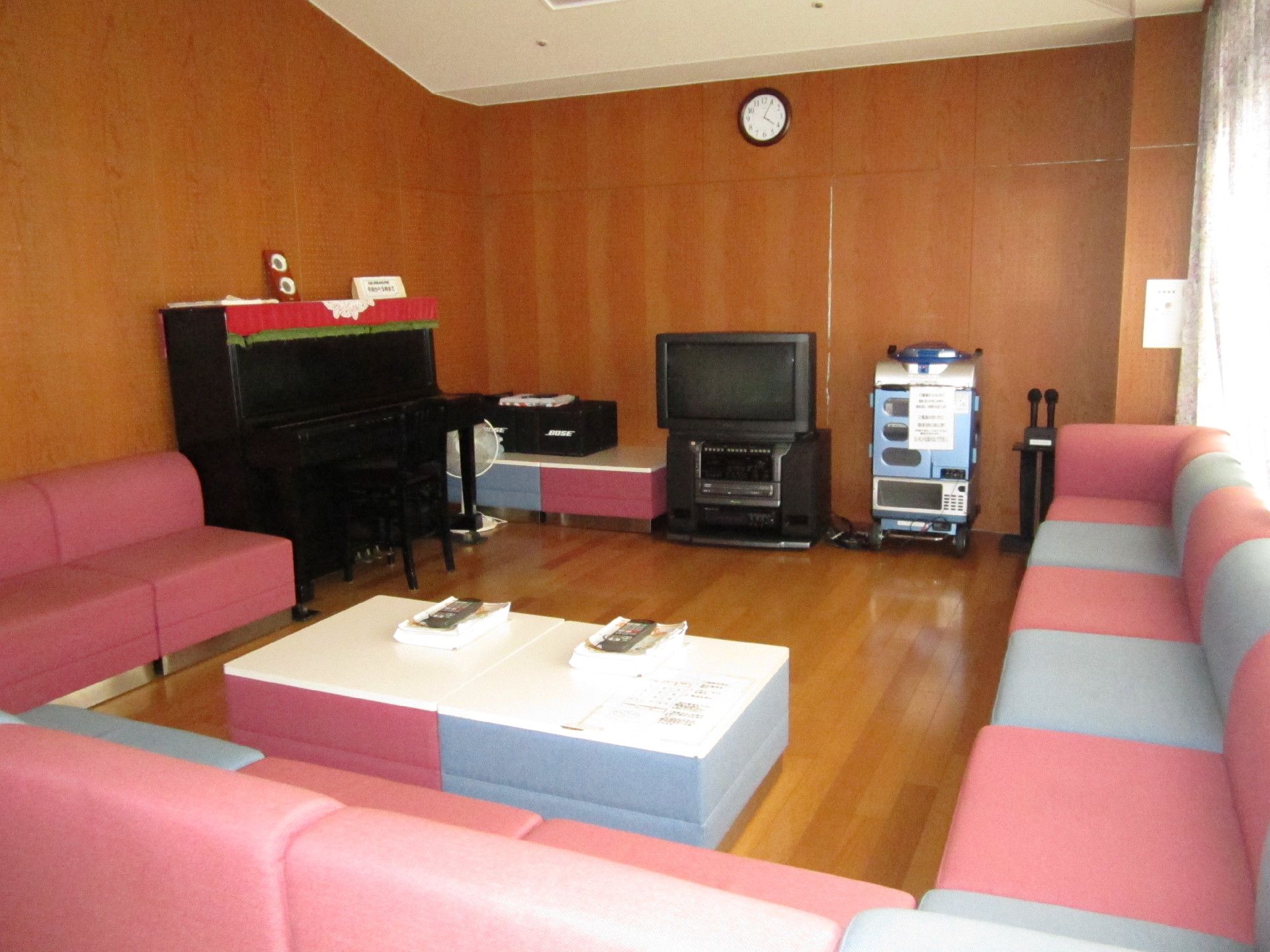 フローリングの部屋に、カラフルな椅子がたくさん並んでいる。中央にテーブルがあり、カラオケ用品が置かれている。
