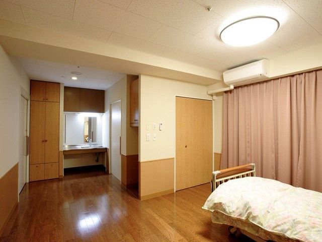 明るい色調のきれいな居室である。ベッドの他に広い洗面台や収納棚などが備え付けられている。エアコンも完備されている。