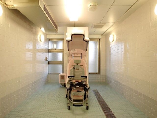 白いタイル張りの清潔感のある浴室。全体はゆったりと広く、座ったまま入浴することができる介護浴槽が置かれている。