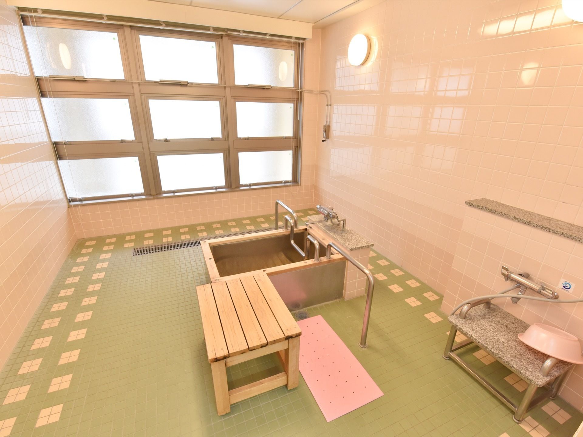 ピンクを基調とした広さが十分にある温かみのある浴室である。中央に浴槽があり、しっかりとした手すりが完備されている。