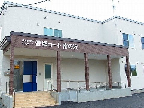 ２階建ての建物の玄関前は広々とした屋根を設置し、側面のダークブラウンの背景に白文字で施設名を表示している。