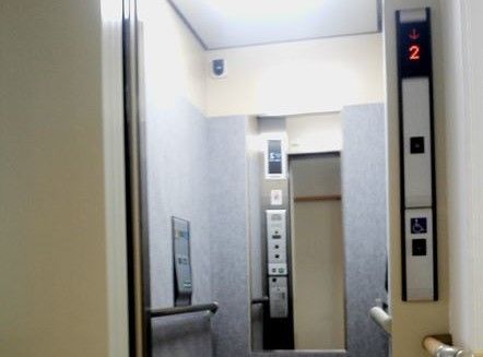 エレベーター内の壁には防護シートが貼られており、両側に手すりが設けられている。その上にエレベーターのボタンが設置されている。