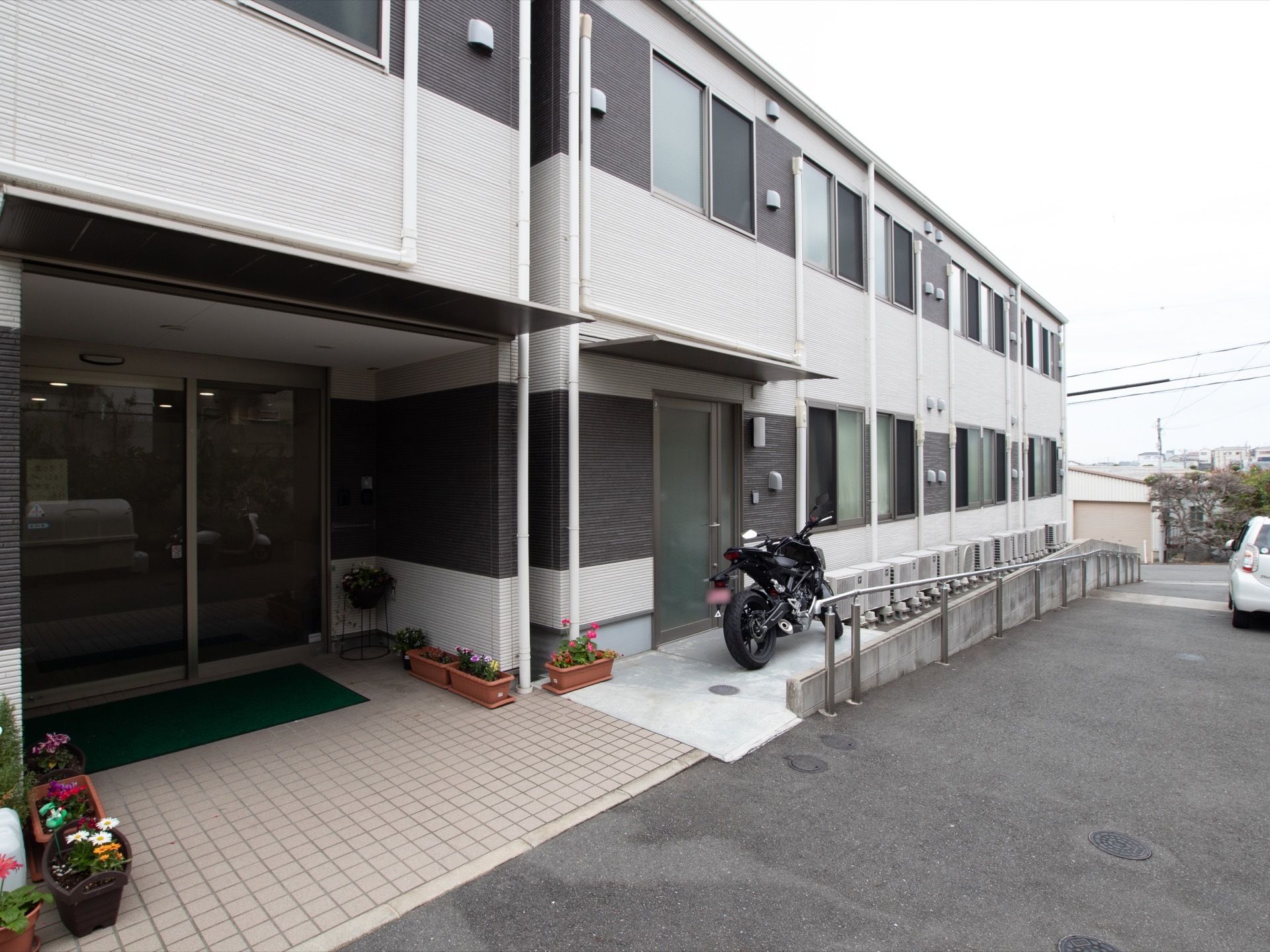 入口には、プランターにかわいらしい花が植えられ置かれている。道路へは手すりとゆるやかなスロープが設置されている。