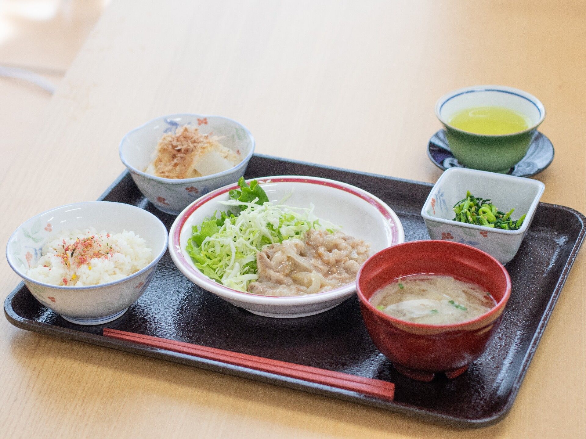 お盆の上に食事が用意されている。ご飯の上にはふりかけがかかっている。その他には味噌汁とおかずが3品置かれている。