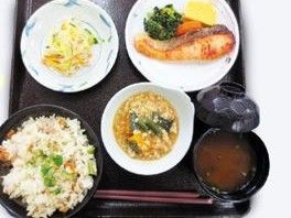 黒いお盆の上に、ご飯、お味噌汁を含む5品の食事が配膳されている。焼鮭のお皿にはブロッコリーや人参もある。
