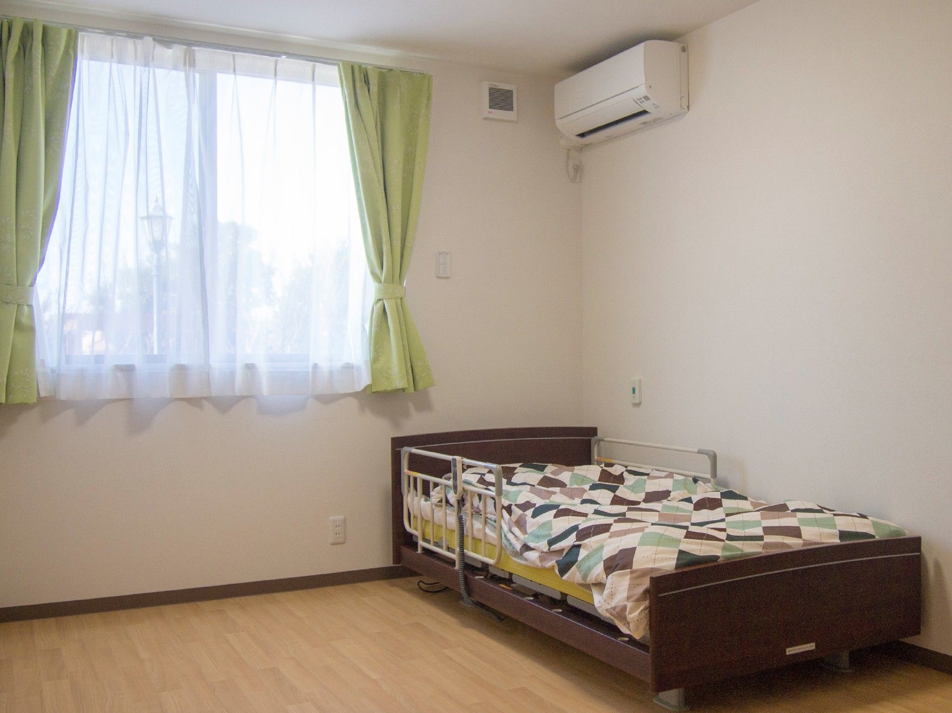 ベッドが置いてあるエアコン付きの小さな部屋の様子。窓があるワンルームタイプの部屋の写真