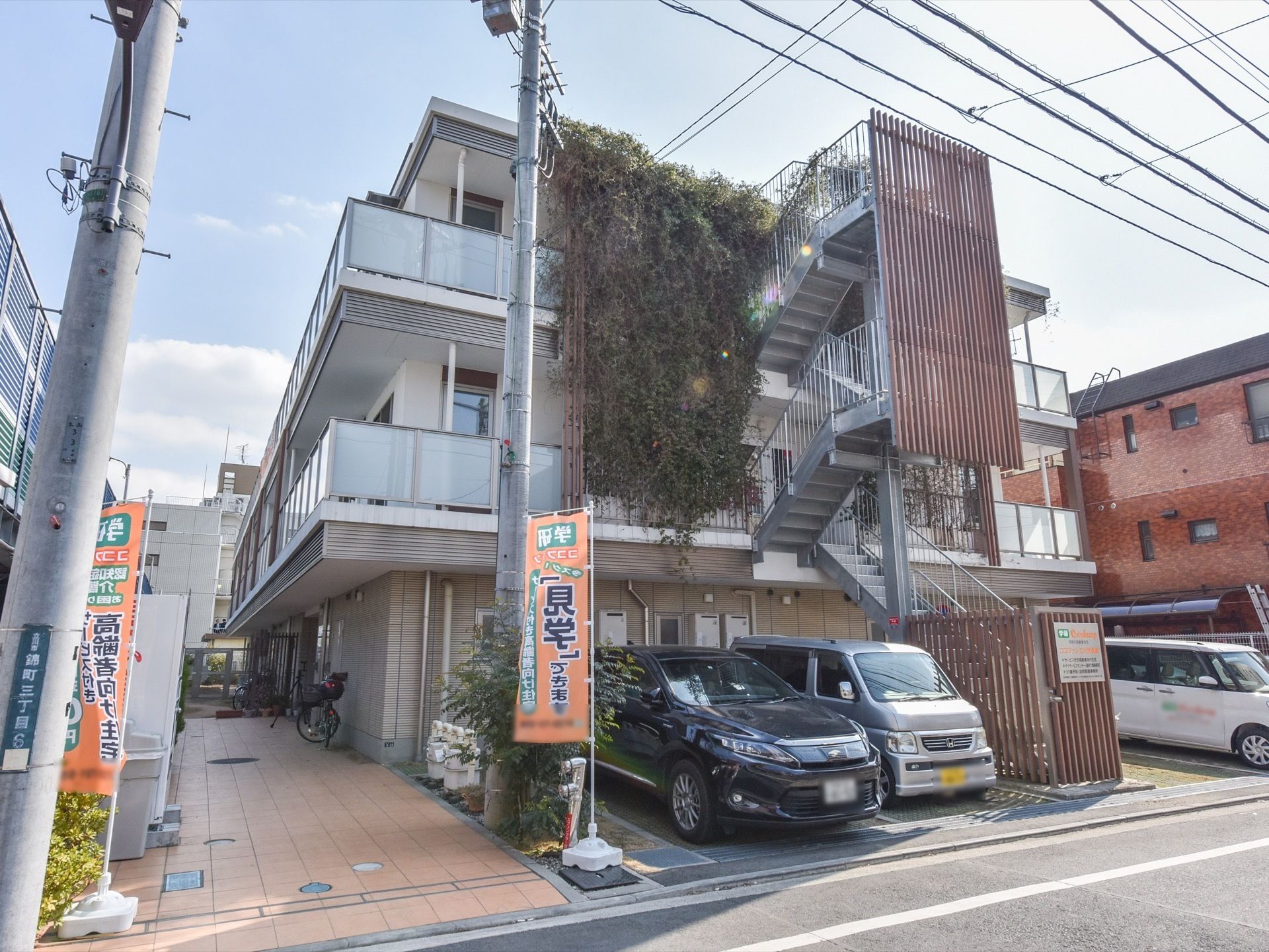 白を基調とした外観の３階建て建物である。建物の中央部分に階段が突き出ており、両側に車を停められるスペースがある。