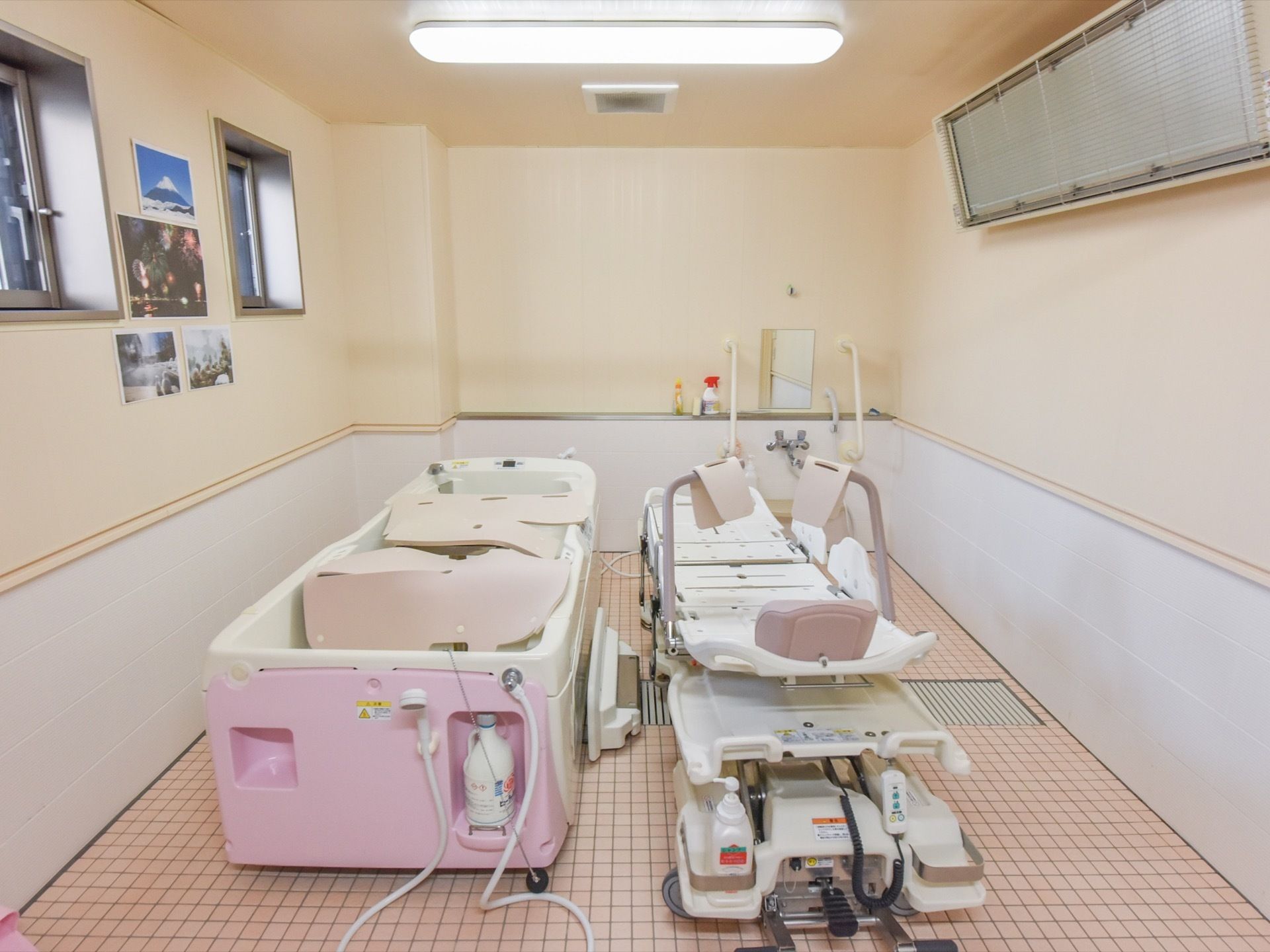 ピンクのタイルの床の上に、寝た体勢で入浴ができる機械浴を設置している。横側の上部に小さな窓が並んでいる。