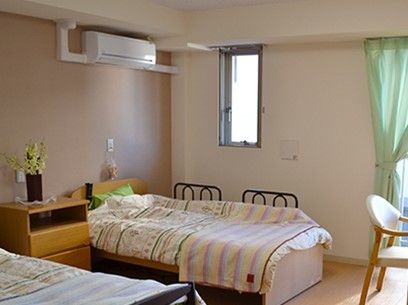 エアコンとベッド、収納家具などが設置された部屋。カーテンがありベランダらしき場所につながっている