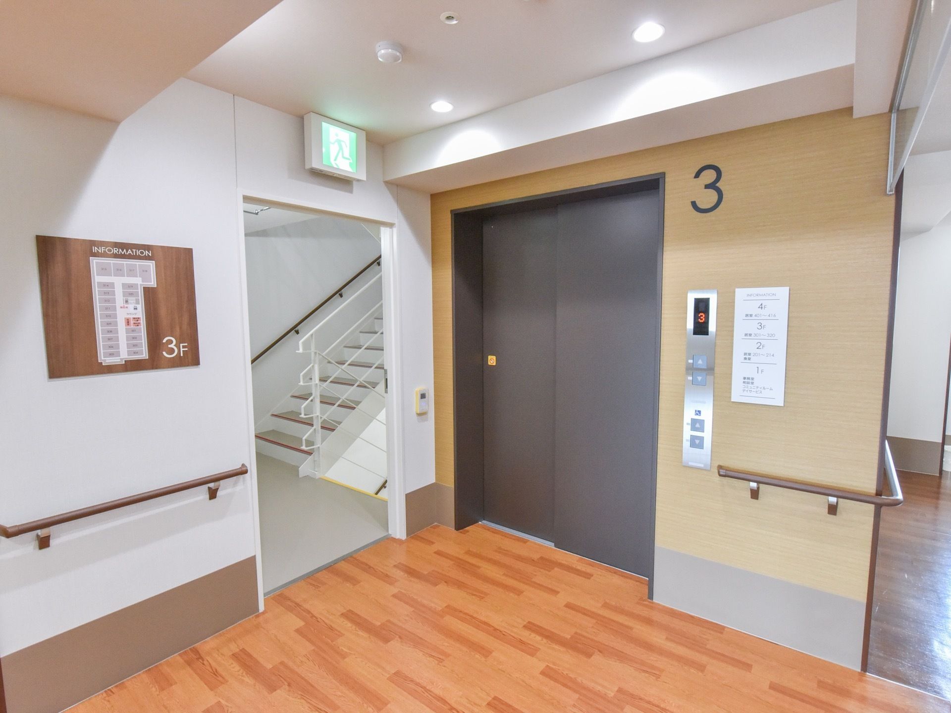 床は木目調になっており、壁には手すりや施設の案内図が設置されている。側のドアは開いており、奥に階段が見える。