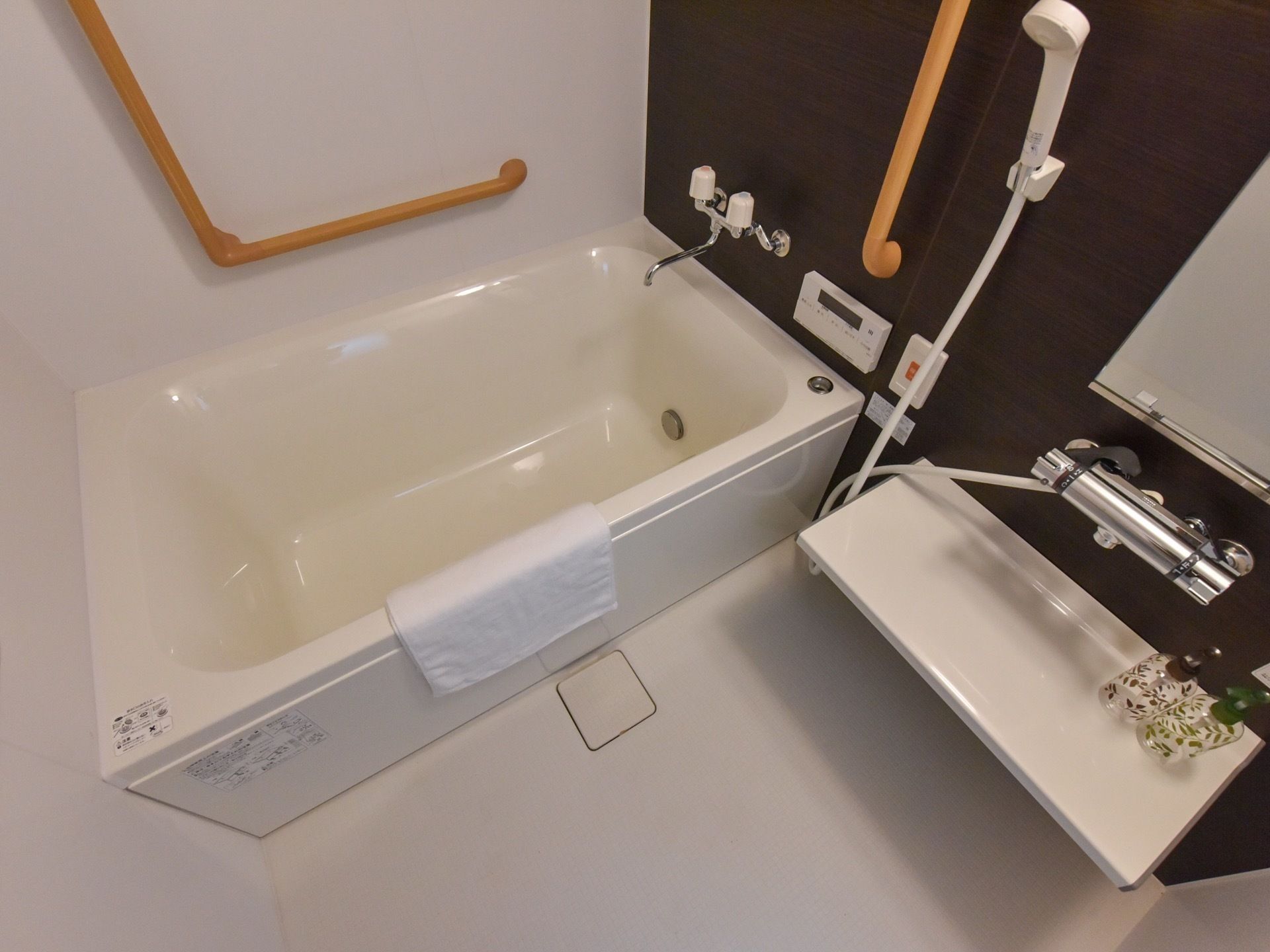 白と茶色を基調としたユニットバスになっていて、浴槽にはタオルが掛けられている。壁にはI字型や、L字型の手すりが取りつけられている。