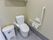 洋式のトイレで、壁には手すりや緊急時呼び出しブザーが取りつけられている。便器の横には可動式の手すりも備わっている。