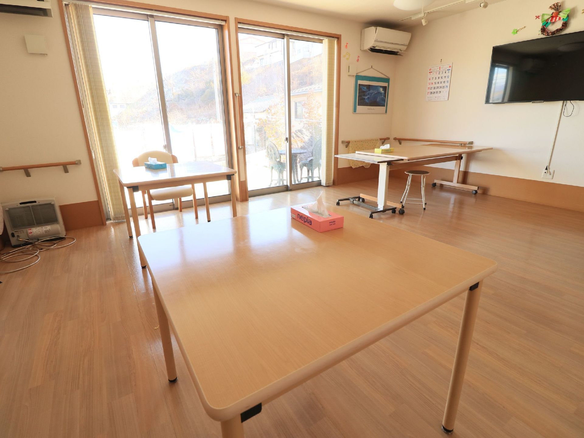 大きな窓からは庭を眺めることができる。壁に液晶テレビとエアコンが設置されている。段差のないフローリングである。