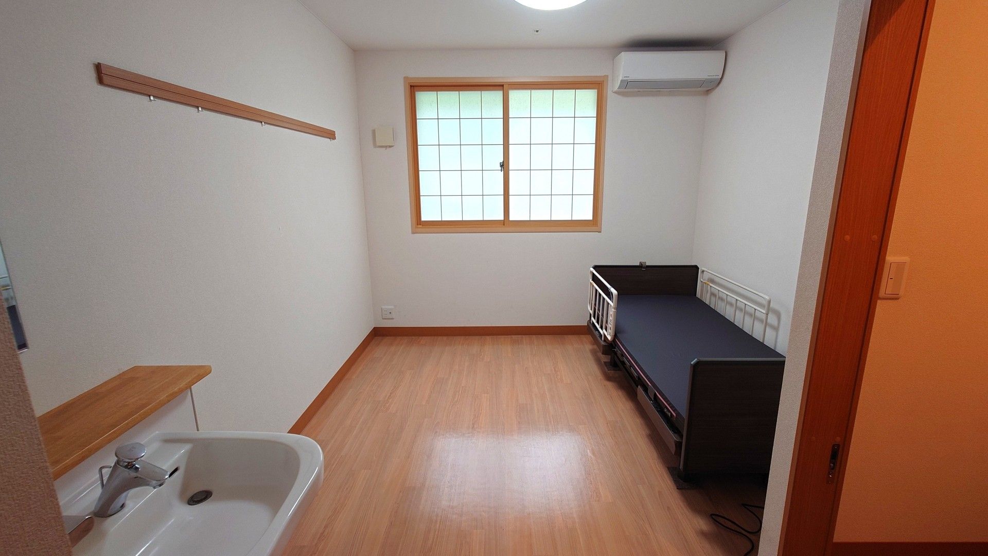 洗面台の奥に落下防止機能の付いたベッドが配置され、腰高の窓がある居室