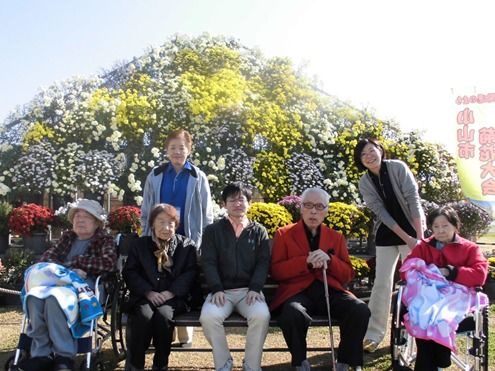 たくさんの花の前で記念撮影を行う入居者様とスタッフ