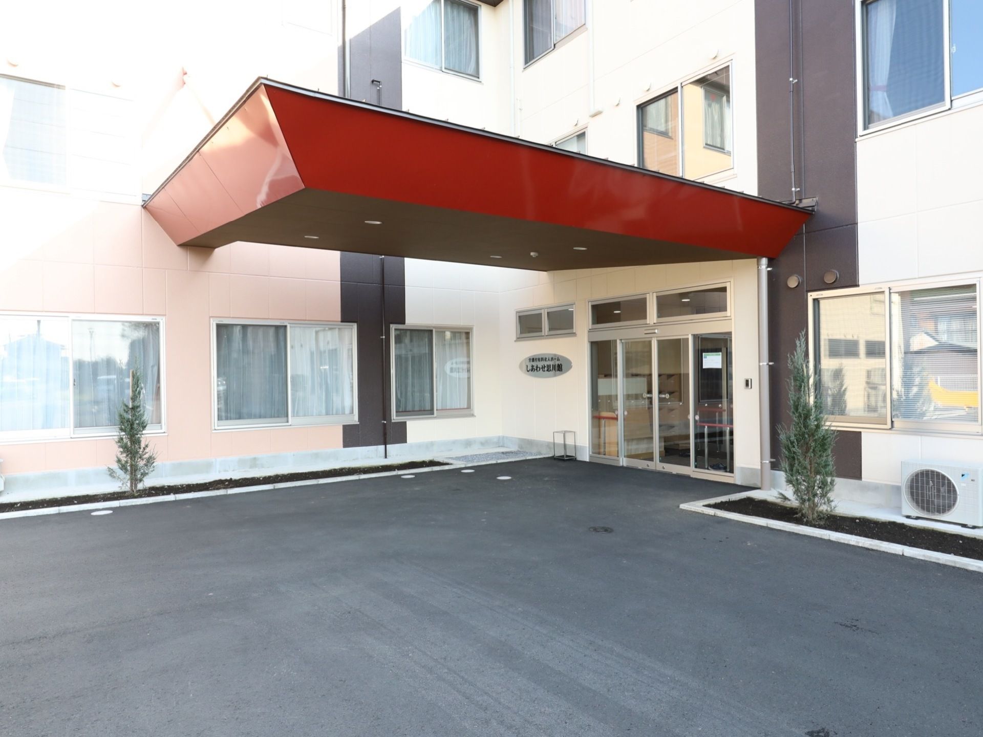 L字型の建物の中心部に設けられた玄関には、大きな赤いひさしが設置されている。玄関の周りには植え込みがあり、緑が楽しめるよう配慮されている。