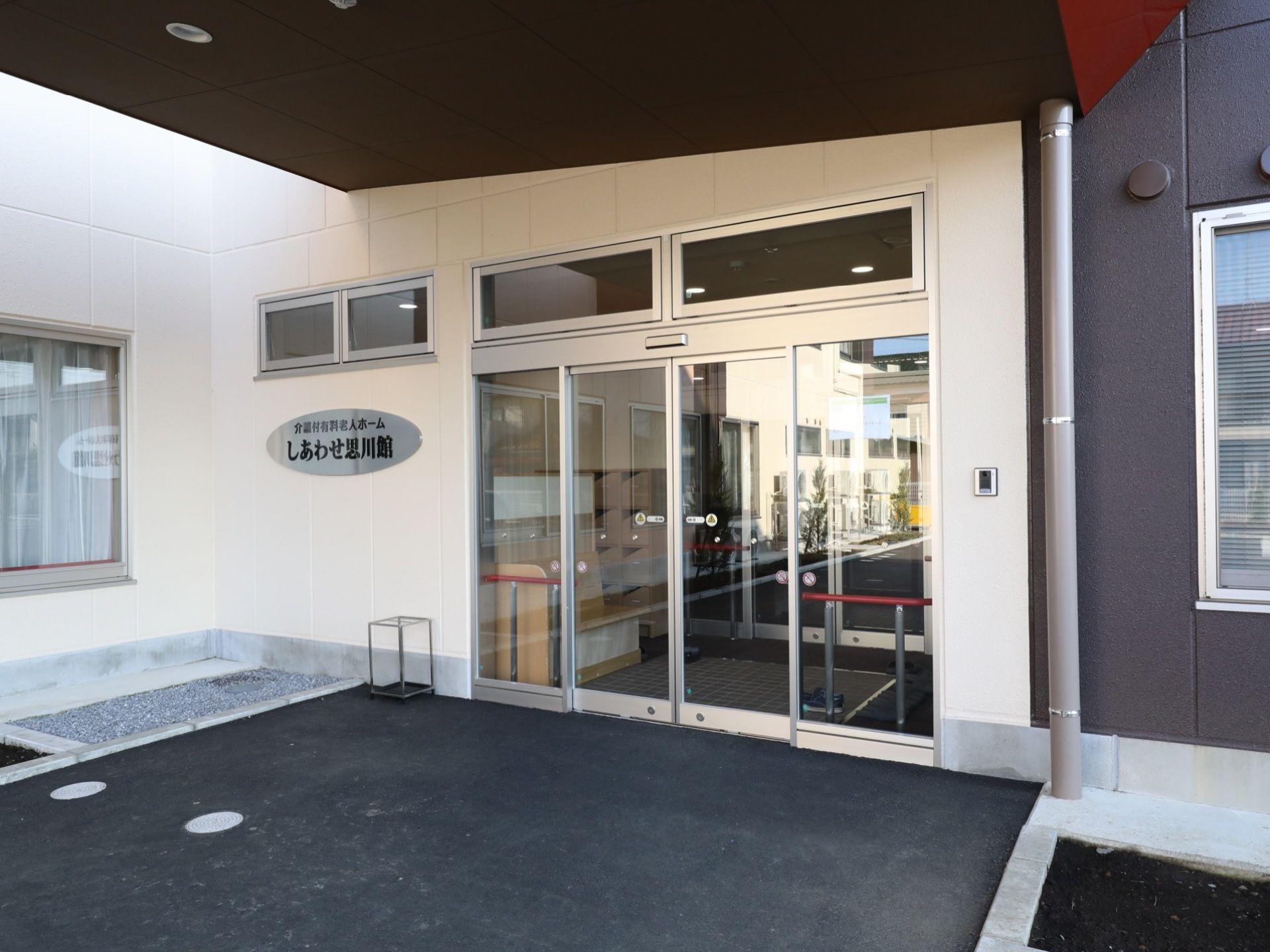 玄関は自動ドアになっており、内部には手すりと受付カウンターが見える。玄関横の壁には施設名の書かれた表札が設置されている。