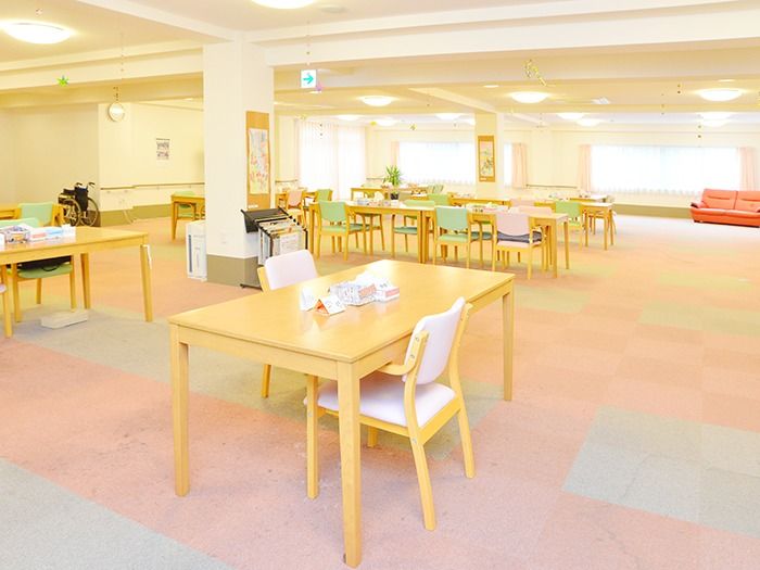 カーペット敷きの広々とした食堂。食事用のテーブルや、赤いソファーが置かれている。