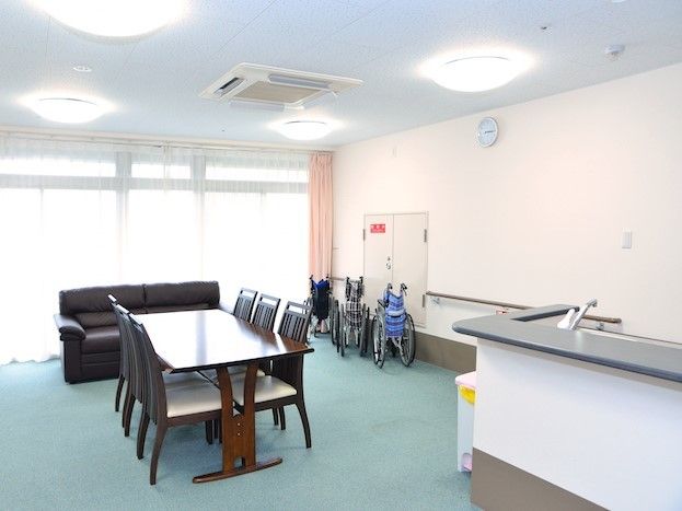 茶色い木製の机といすが置かれている部屋。奥には黒いソファが置かれている