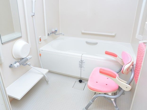 一人用の浴槽がある浴室。至る所に手すりが設置されており、ピンク色の椅子も置かれている。