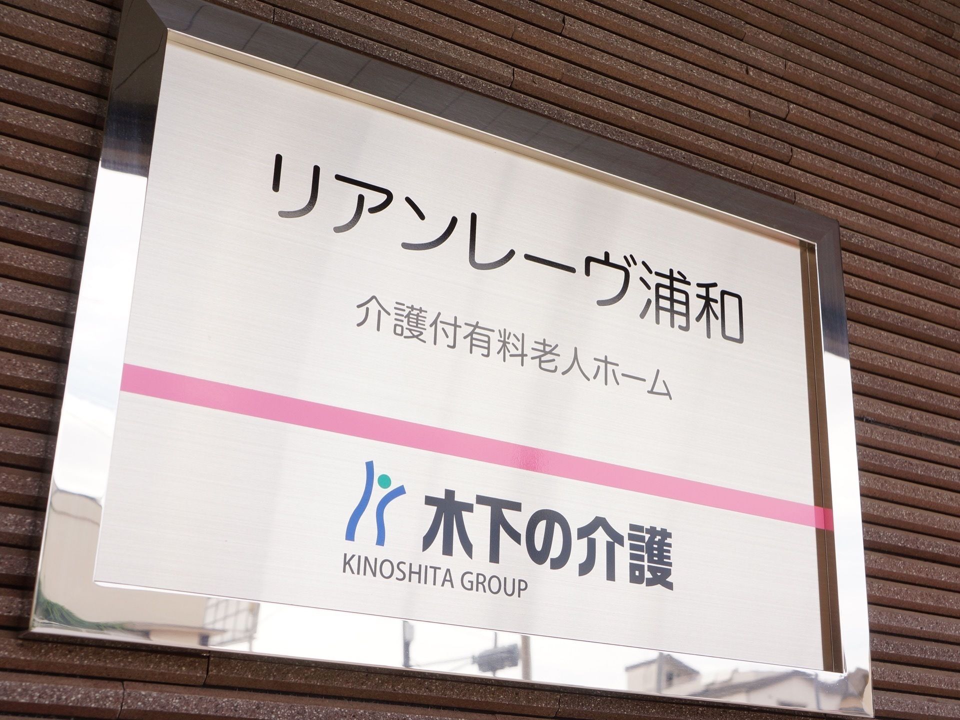 ピンクのラインの上下に、黒字で施設名と会社名が記載された看板
