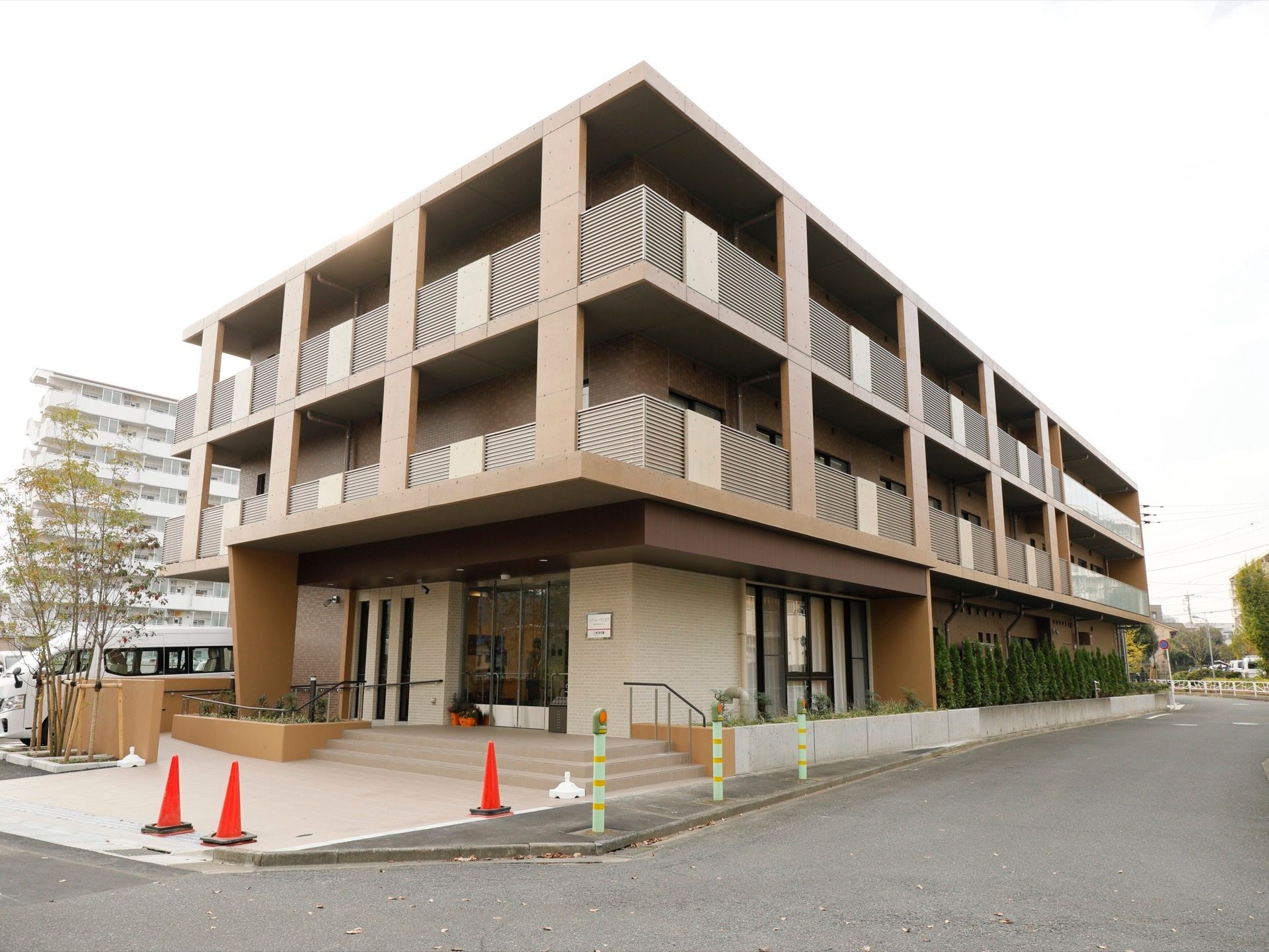 ベージュ系でまとめられたシンプルな外観をしている。花壇には木が植えられており、玄関までは階段だけではなくスロープも用意されている。