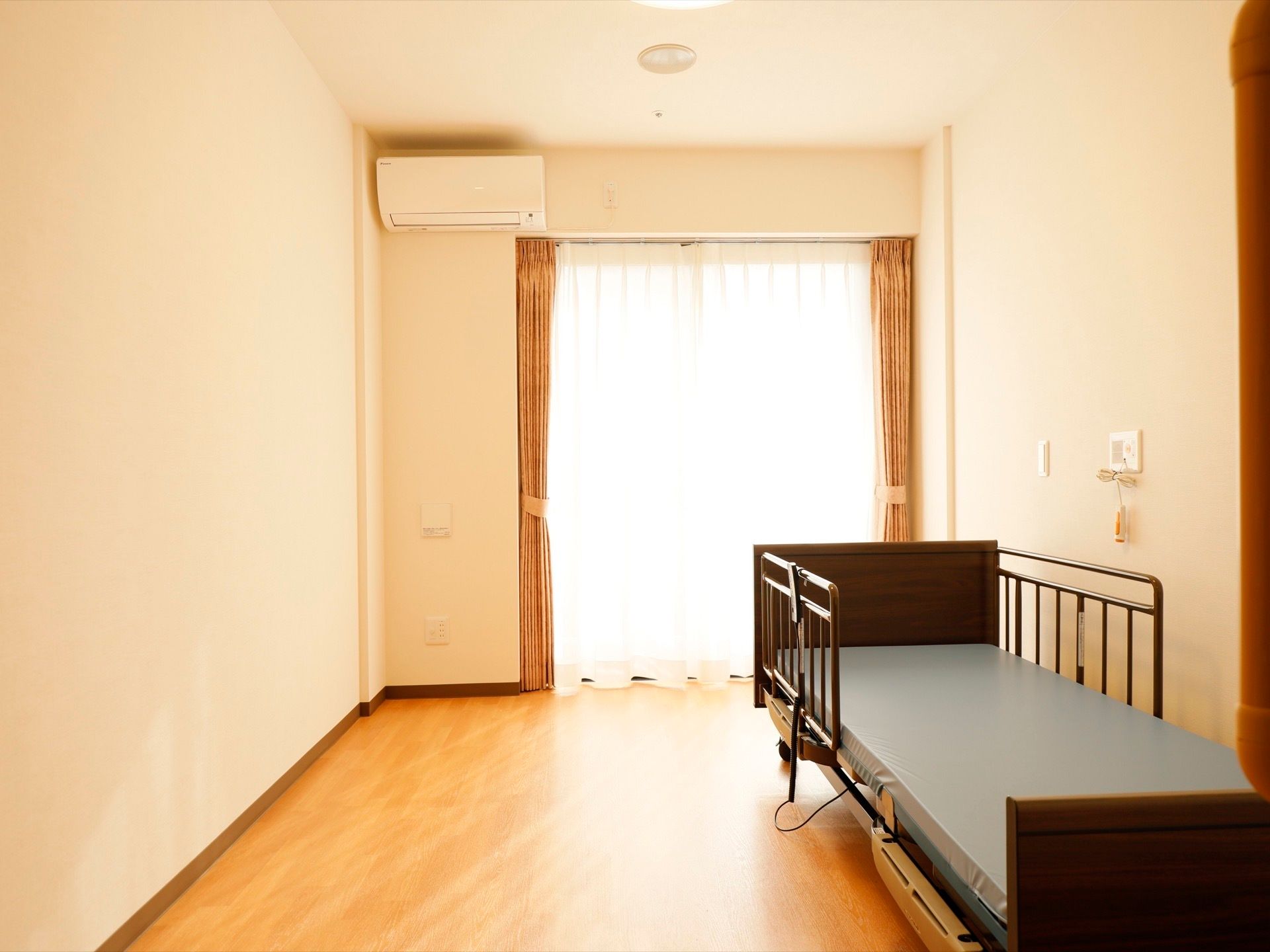 居室には濃いブラウンの介護用ベッドが置かれている。窓が大きく取られており、呼び出しボタンやエアコンも備えつけられている。