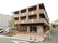 落ち着いた色合いが印象的な、３階建ての施設である。階段やスロープが完備されている。駐車場には、車が数台停まっている。