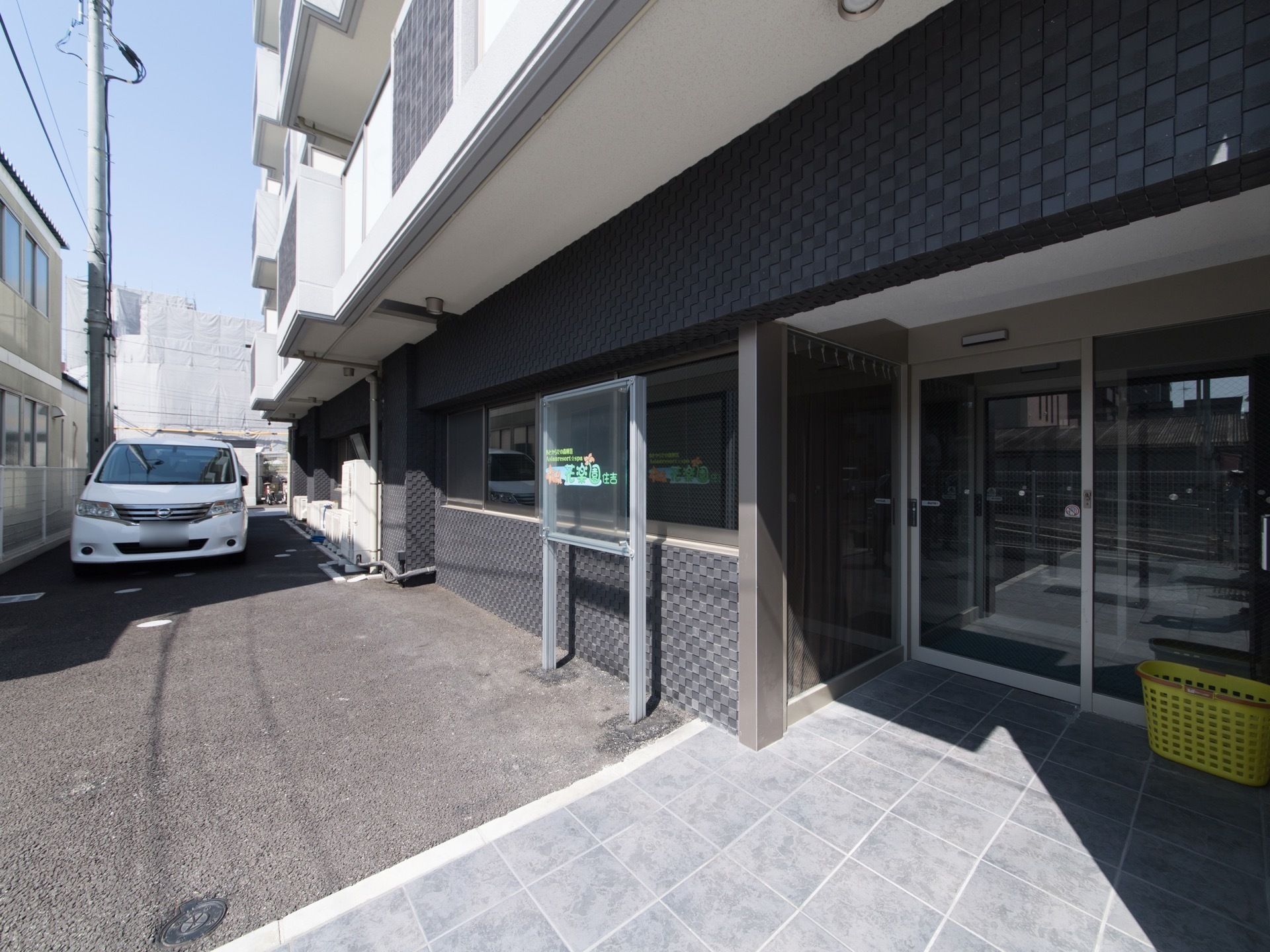 マンションのような外観に自動ドアが設置されている。通路はタイルが貼られている。建物の前には駐車スペースがある。